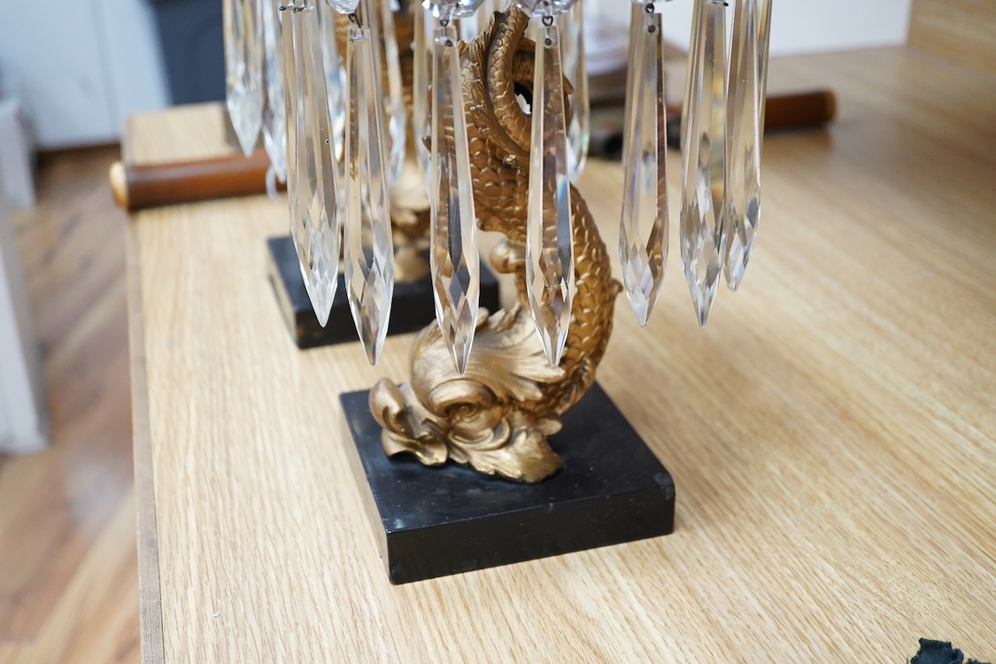 A pair of William IV gilt metal candlesticks, the stems formed as dolphins, with glass lustre drops, raised on square slate bases, 37cm high
